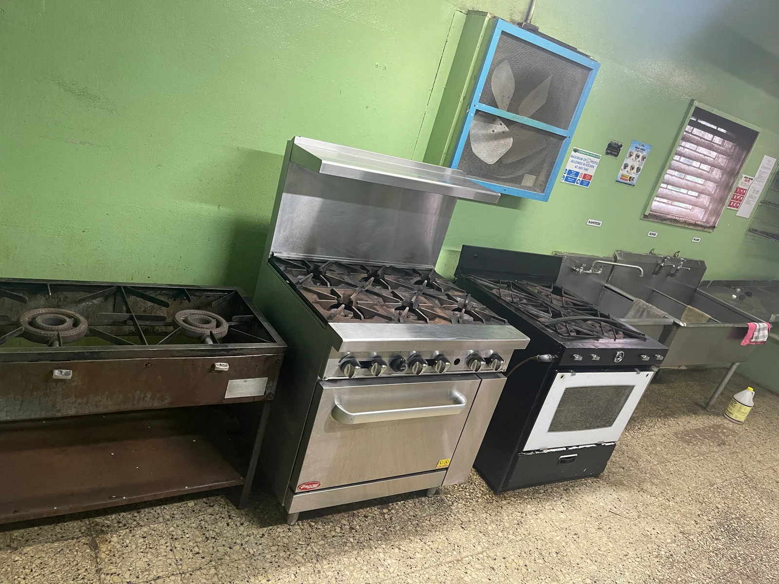 Cooking ranges, sink and wall fan in a kitchen.